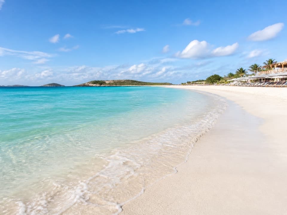 White-sand beach and turquoise water at Orient Beach, with umbrellas and seaside restaurants in the distance.