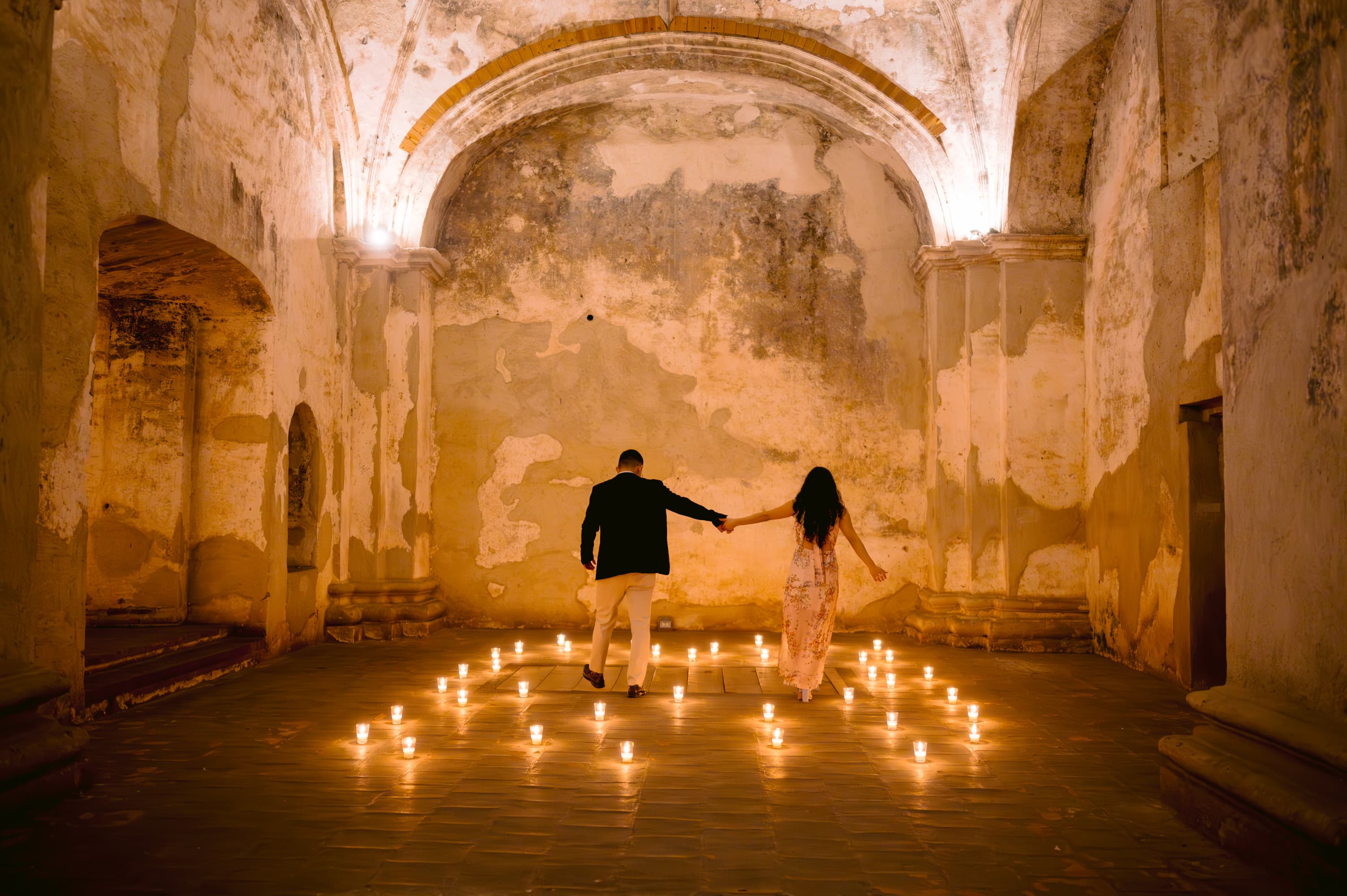 Oscar and Meli walking hand in hand among hundreds of candles, in an old colonial nave in Antigua Guatemala.